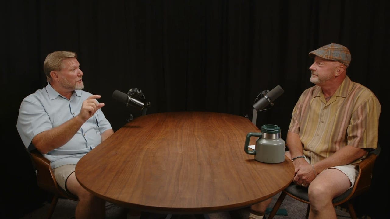 Adam C. Benefield and Ed Tidwell talking across a wooden table in a studio.